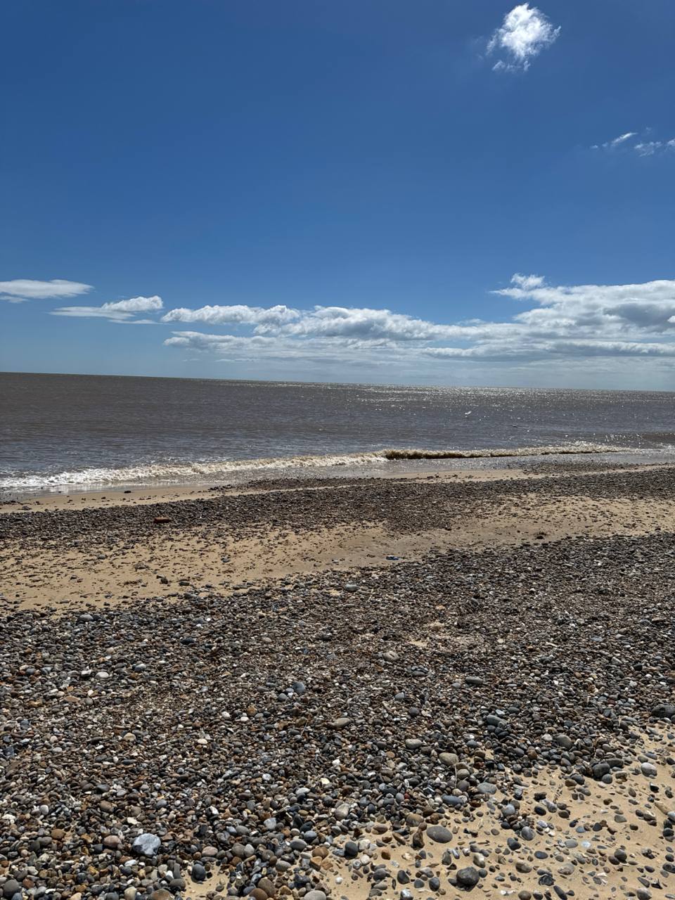 Pebbles, sand, surf, open water, and sky on the Kessingland coast.