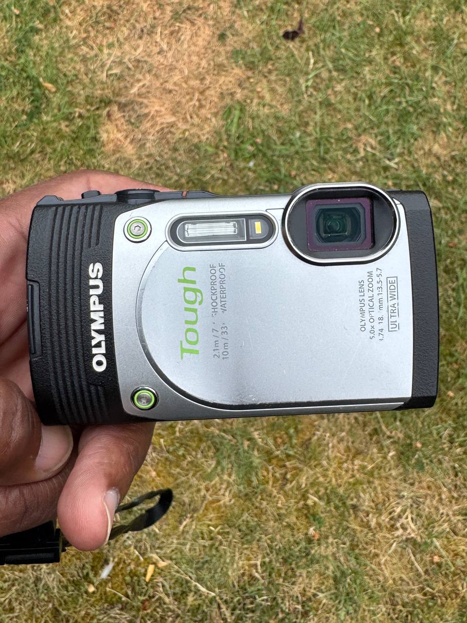An Olympus Tough compact camera held over dry grass